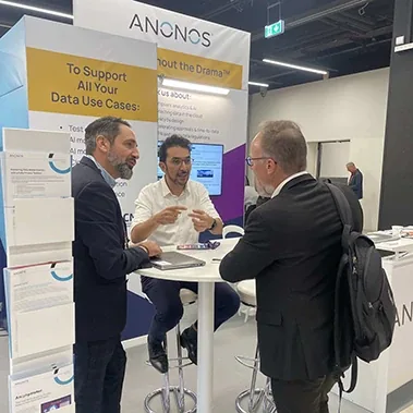 Anonos team members in conversation with an attendee at a conference booth.